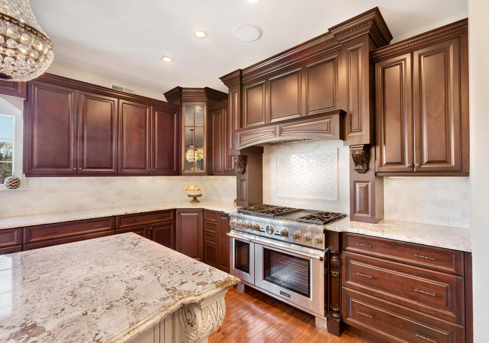 Example of a large classic u-shaped medium tone wood floor eat-in kitchen design in New York with an undermount sink, raised-panel cabinets, brown cabinets, granite countertops, white backsplash, stone tile backsplash, stainless steel appliances and an island