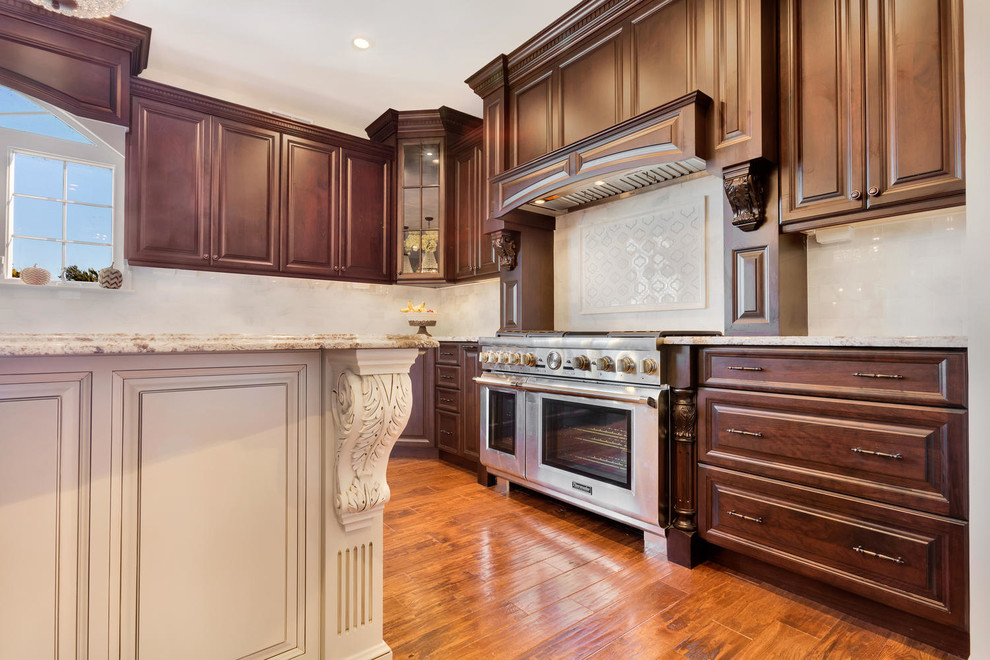 Eat-in kitchen - large traditional u-shaped medium tone wood floor eat-in kitchen idea in New York with an undermount sink, raised-panel cabinets, brown cabinets, granite countertops, white backsplash, stone tile backsplash, stainless steel appliances and an island