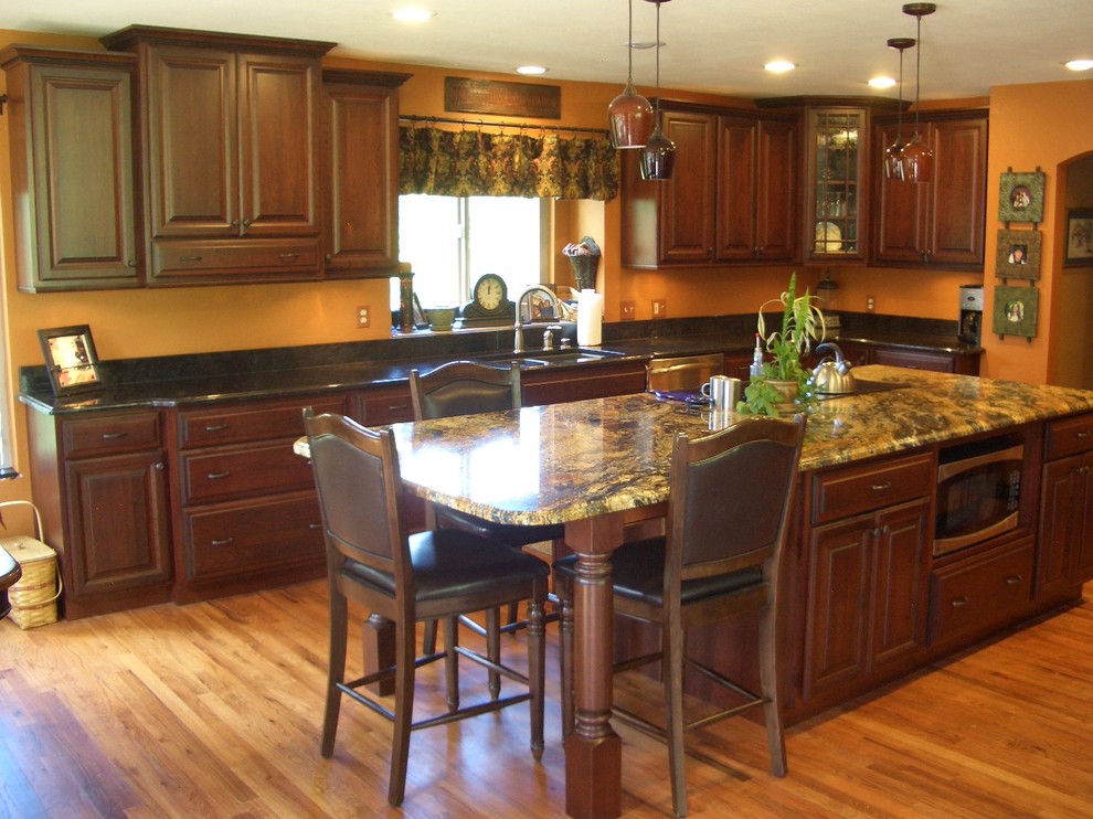 Example of a large classic u-shaped light wood floor and beige floor eat-in kitchen design in Denver with an undermount sink, raised-panel cabinets, dark wood cabinets, granite countertops, stainless steel appliances, an island, black backsplash, stone slab backsplash and black countertops