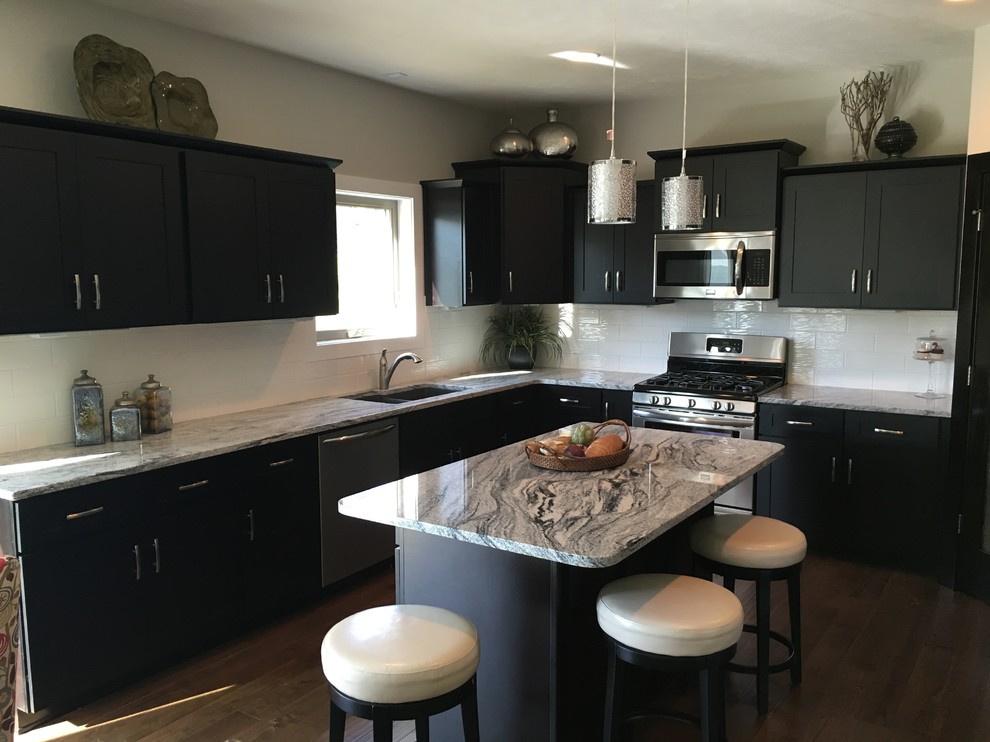 Medium sized contemporary u-shaped kitchen/diner in Omaha with a belfast sink, shaker cabinets, dark wood cabinets, granite worktops, white splashback, ceramic splashback, stainless steel appliances, dark hardwood flooring and an island.