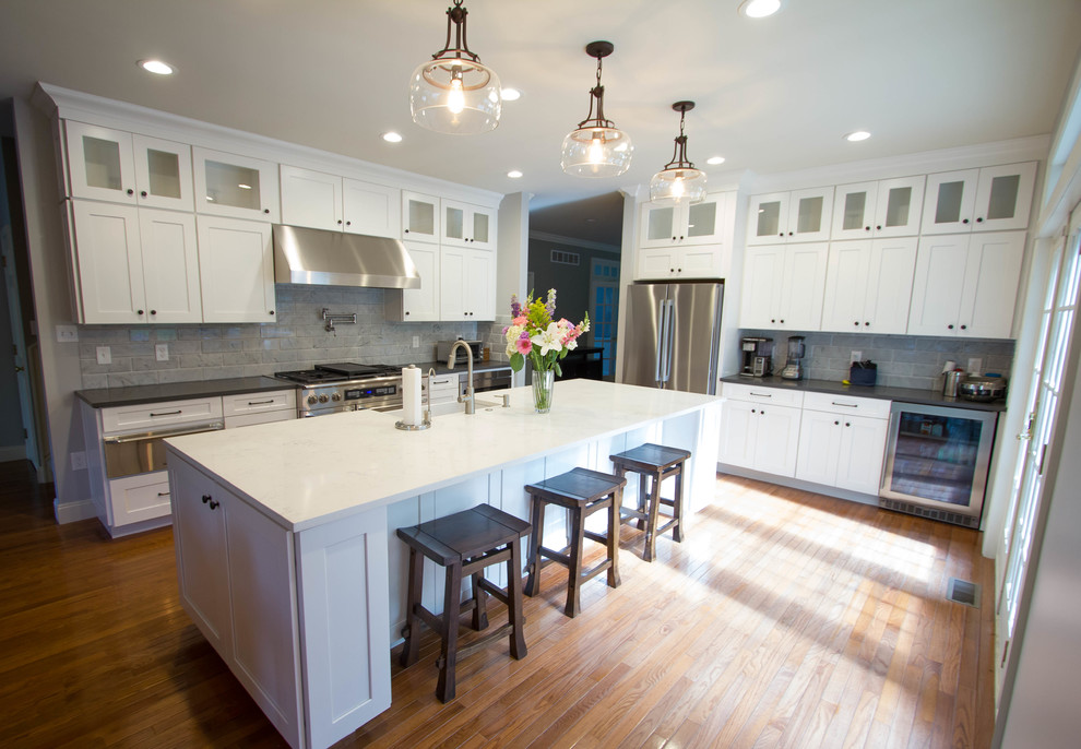 Eat-in kitchen - large transitional l-shaped medium tone wood floor and orange floor eat-in kitchen idea in Philadelphia with a farmhouse sink, shaker cabinets, white cabinets, quartz countertops, white backsplash, marble backsplash, stainless steel appliances and an island
