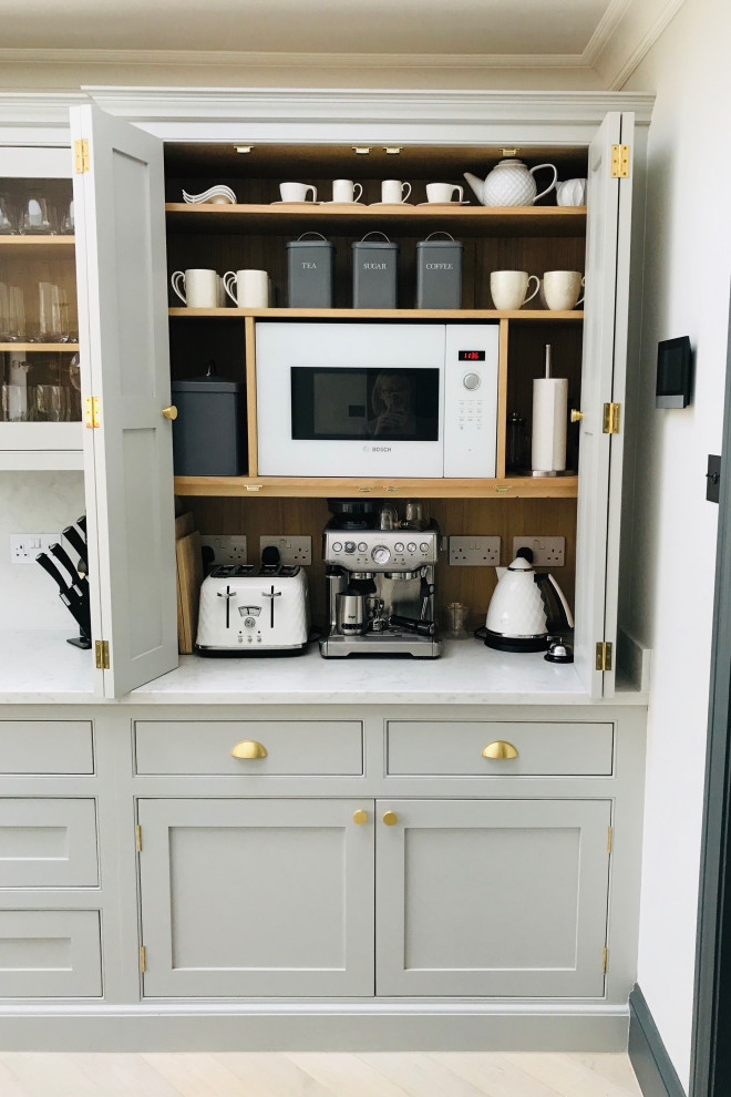 Cette photo montre une cuisine américaine chic en L de taille moyenne avec un placard à porte affleurante, des portes de placard beiges, un plan de travail en quartz, îlot et un plan de travail blanc.