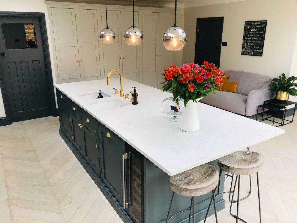 Dark green kitchen island with white worktops, builtin sink and gold