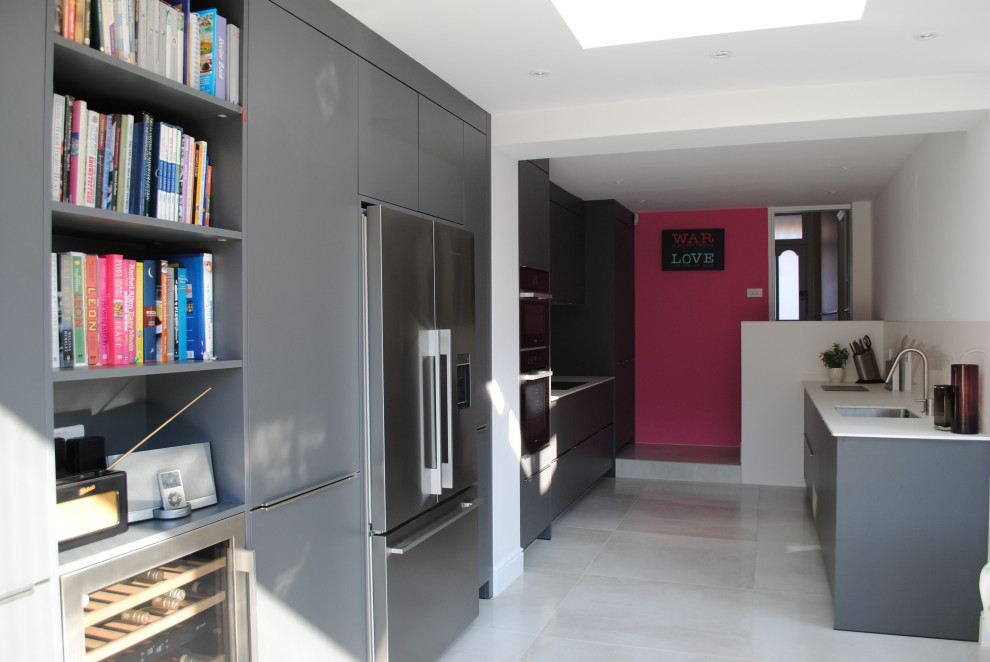 This is an example of a large contemporary galley kitchen/diner in London with a built-in sink, flat-panel cabinets, grey cabinets, composite countertops, pink splashback, glass sheet splashback, stainless steel appliances, porcelain flooring, grey floors and white worktops.