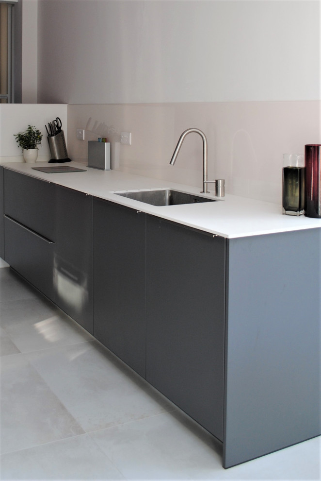 Design ideas for a large contemporary galley kitchen/diner in London with a built-in sink, flat-panel cabinets, grey cabinets, composite countertops, pink splashback, glass sheet splashback, stainless steel appliances, porcelain flooring, grey floors and white worktops.
