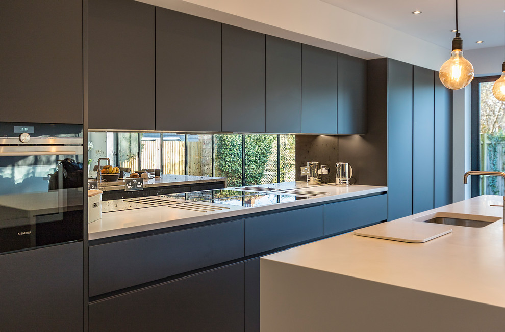 Example of a large minimalist single-wall ceramic tile and gray floor open concept kitchen design in Surrey with a drop-in sink, flat-panel cabinets, gray cabinets, solid surface countertops, metallic backsplash, mirror backsplash, black appliances and an island