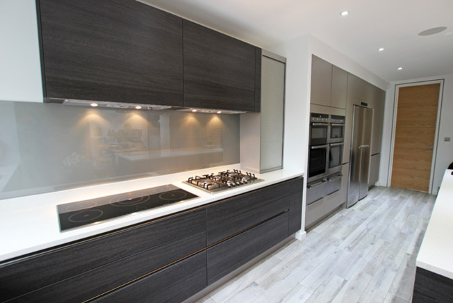 Moderne Küche mit schwarzen Schränken, Küchenrückwand in Metallic, Glasrückwand und Kücheninsel in London