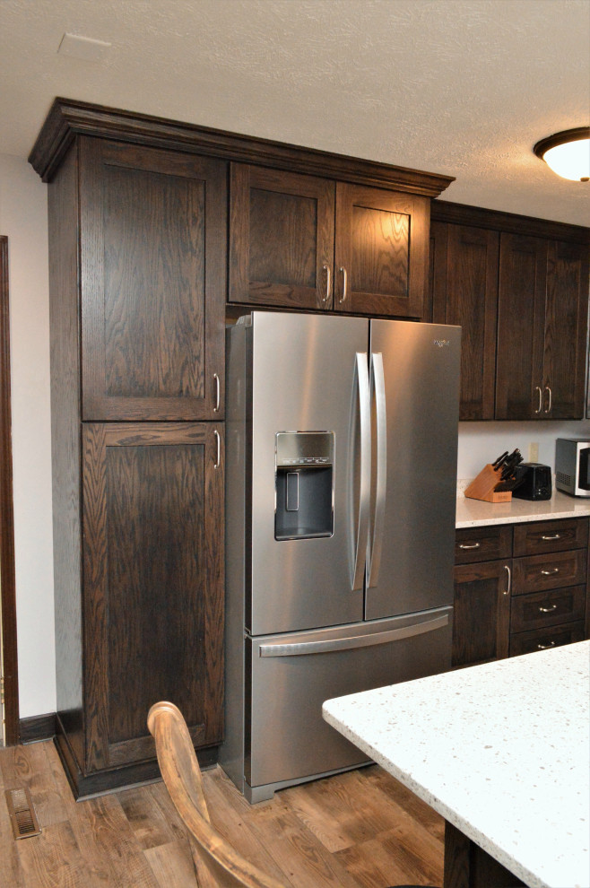 Photo of a medium sized rustic l-shaped open plan kitchen in Chicago with a submerged sink, shaker cabinets, dark wood cabinets, quartz worktops, stainless steel appliances, laminate floors, an island, brown floors and grey worktops.