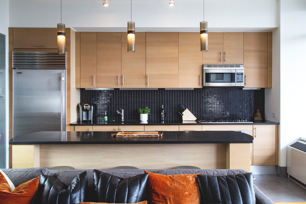 Modern inredning av ett svart linjärt svart kök med öppen planlösning, med en nedsänkt diskho, skåp i ljust trä, bänkskiva i onyx, svart stänkskydd, stänkskydd i mosaik, rostfria vitvaror, klinkergolv i porslin, en köksö och grått golv
