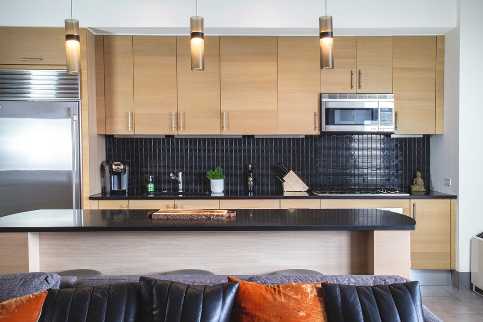 Modern inredning av ett svart linjärt svart kök med öppen planlösning, med en nedsänkt diskho, skåp i ljust trä, bänkskiva i onyx, svart stänkskydd, stänkskydd i mosaik, rostfria vitvaror, klinkergolv i porslin, en köksö och grått golv