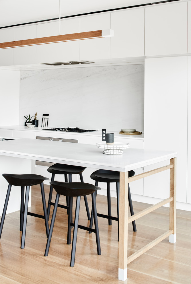 Foto de cocina moderna con armarios con paneles lisos, puertas de armario blancas, salpicadero blanco, electrodomésticos de acero inoxidable, suelo de madera clara y una isla