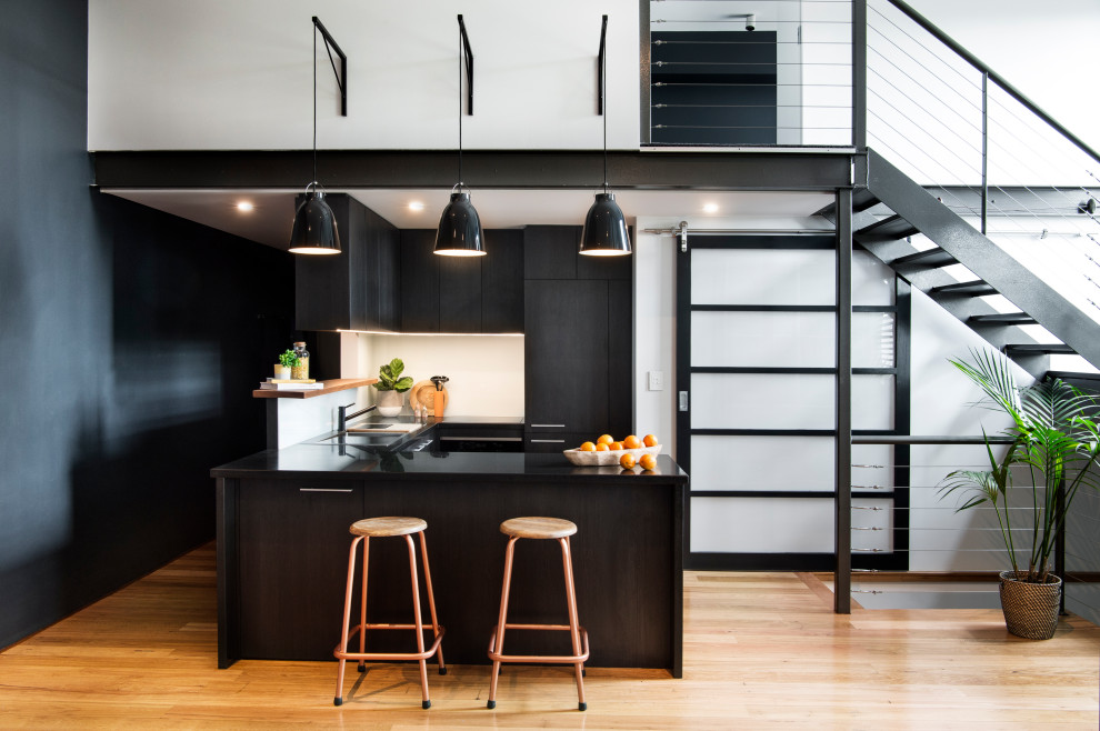 Small urban u-shaped medium tone wood floor eat-in kitchen photo in Sydney with a drop-in sink, white backsplash, glass sheet backsplash, black appliances, a peninsula and black countertops