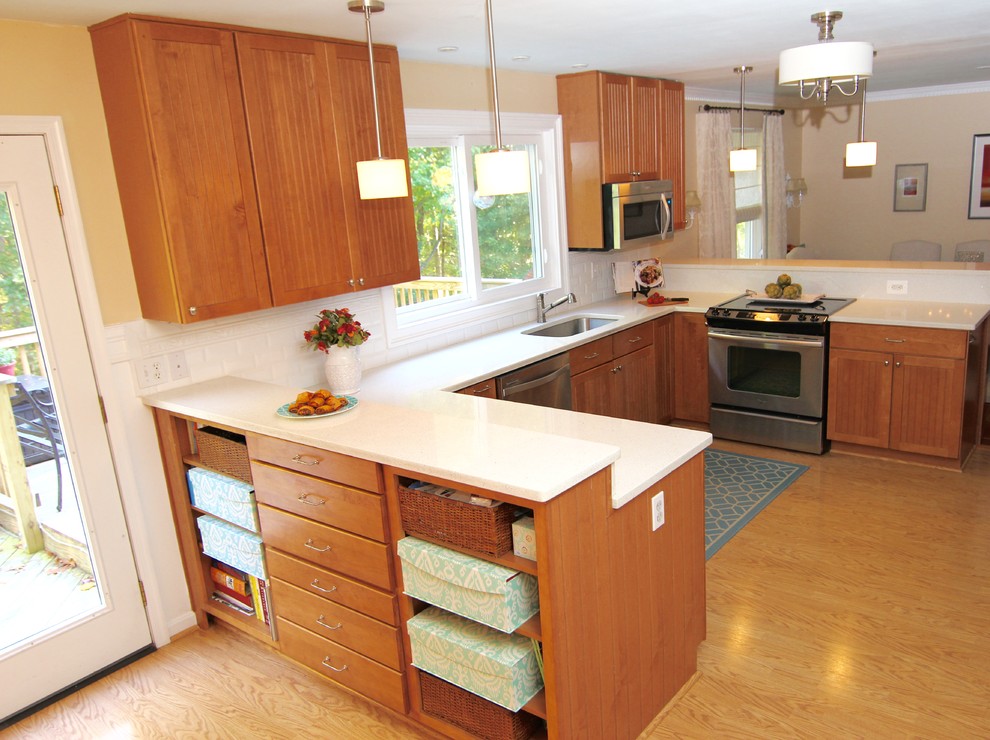 Inspiration for a mid-sized timeless u-shaped light wood floor eat-in kitchen remodel in DC Metro with an undermount sink, medium tone wood cabinets, quartz countertops, white backsplash, ceramic backsplash, stainless steel appliances, glass-front cabinets and a peninsula