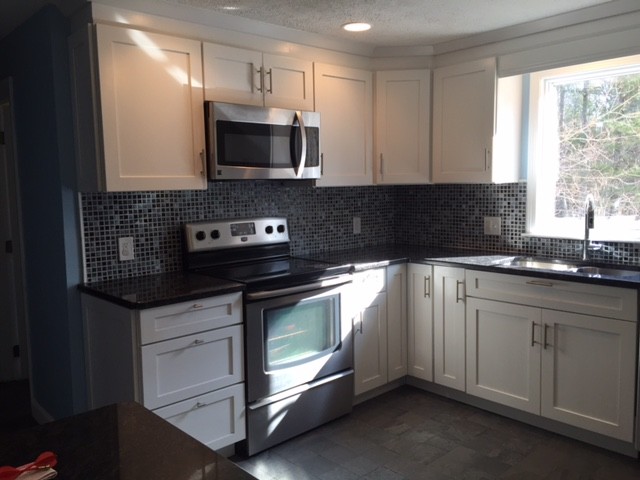 Example of a mid-sized transitional l-shaped porcelain tile enclosed kitchen design in Boston with an undermount sink, shaker cabinets, white cabinets, granite countertops, gray backsplash, mosaic tile backsplash, stainless steel appliances and a peninsula