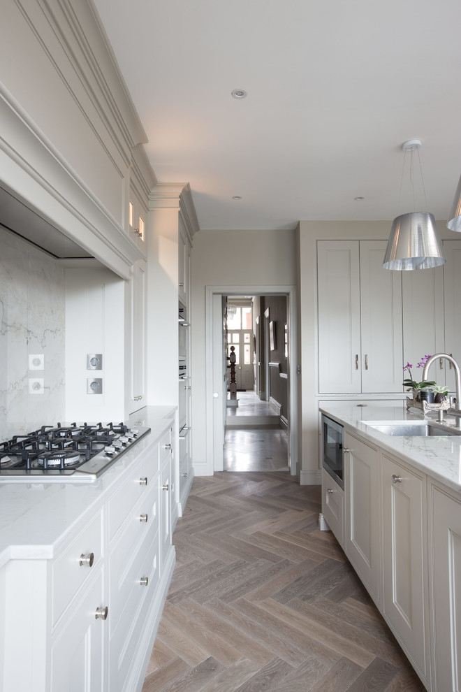 Cette image montre une cuisine ouverte design en L avec un placard à porte shaker, des portes de placard grises, plan de travail en marbre, une crédence en dalle de pierre, un sol en bois brun et îlot.