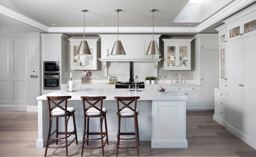 Kitchen - transitional l-shaped light wood floor kitchen idea in Dublin with an undermount sink, recessed-panel cabinets, white cabinets, white backsplash, stone slab backsplash and an island