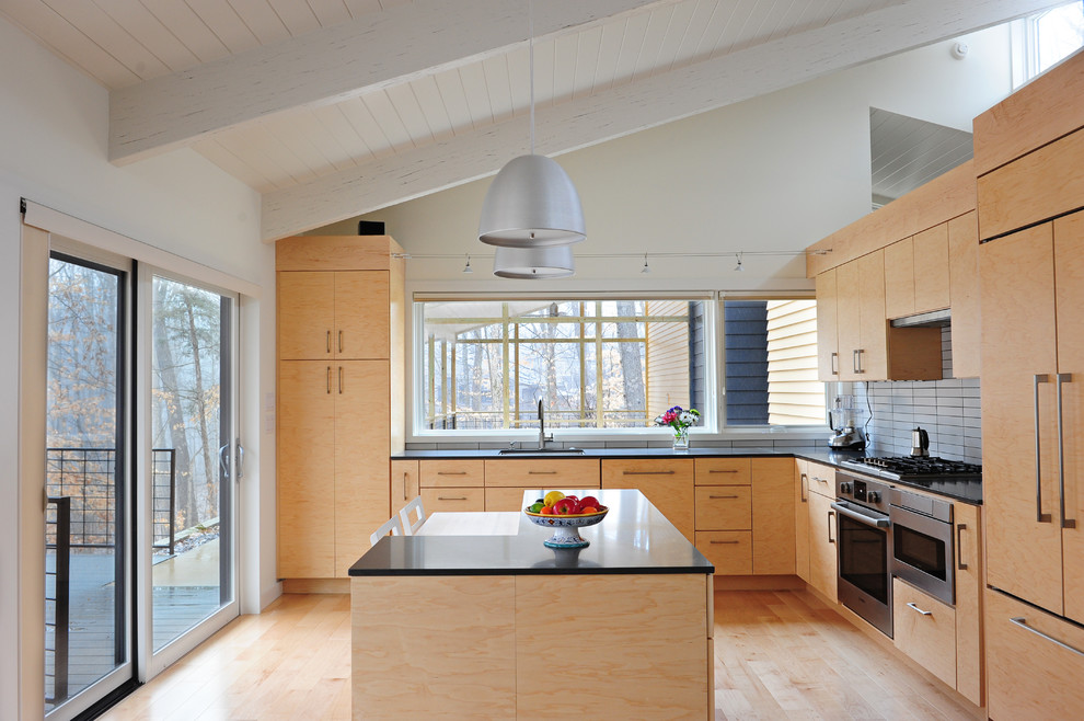 Bild på ett funkis l-kök, med en undermonterad diskho, släta luckor, skåp i ljust trä, vitt stänkskydd, integrerade vitvaror, ljust trägolv och en köksö