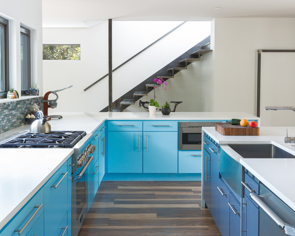 Moderne Küche mit Landhausspüle, flächenbündigen Schrankfronten, blauen Schränken, bunter Rückwand, Rückwand aus Mosaikfliesen, Küchengeräten aus Edelstahl, dunklem Holzboden, Kücheninsel, braunem Boden und weißer Arbeitsplatte in Austin