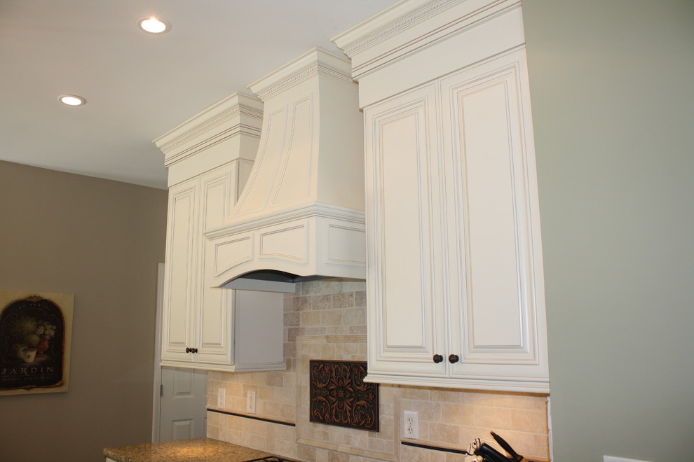 Inredning av ett klassiskt stort kök, med en undermonterad diskho, luckor med upphöjd panel, vita skåp, granitbänkskiva, beige stänkskydd, svarta vitvaror, mörkt trägolv och en köksö
