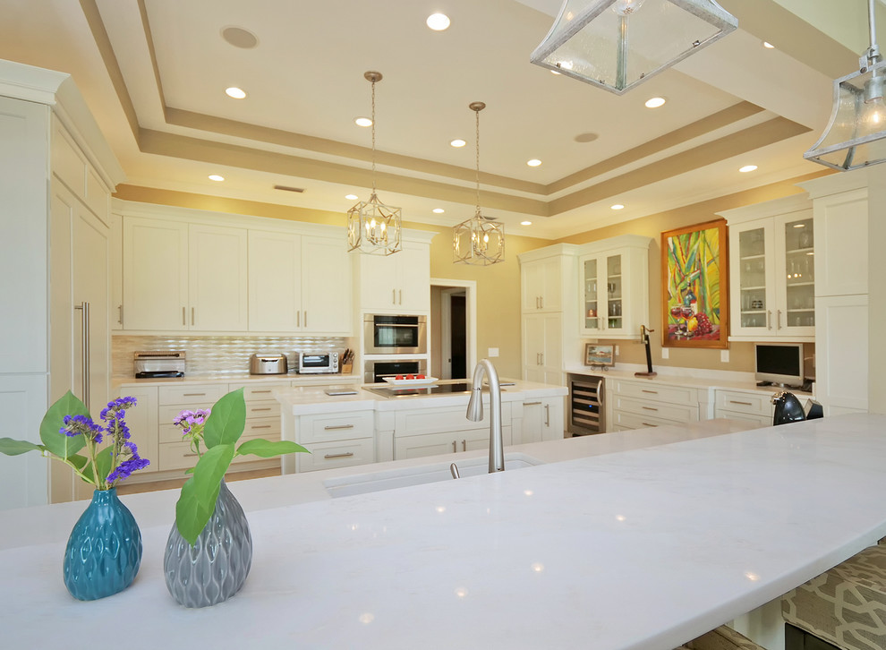 This is an example of an expansive world-inspired u-shaped kitchen/diner in Jacksonville with a submerged sink, beaded cabinets, white cabinets, quartz worktops, beige splashback, marble splashback, stainless steel appliances, porcelain flooring, multiple islands, beige floors and white worktops.