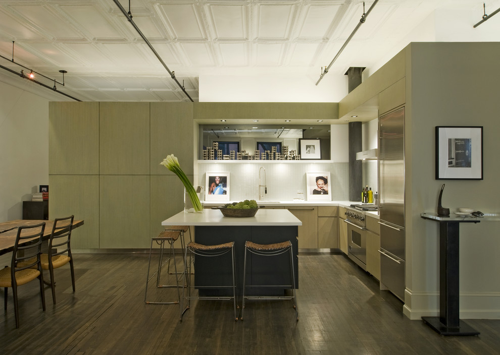 На фото: угловая кухня-гостиная в стиле лофт с плоскими фасадами, столешницей из кварцевого агломерата, белым фартуком, техникой из нержавеющей стали и зелеными фасадами