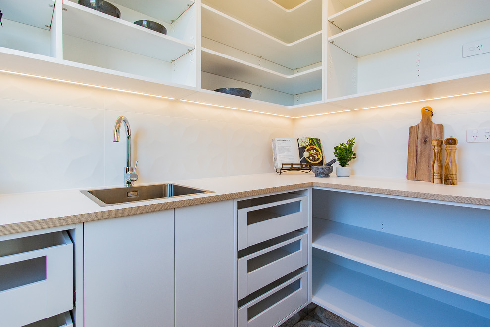Large minimalist l-shaped concrete floor and multicolored floor kitchen pantry photo in Christchurch with flat-panel cabinets, an island, a single-bowl sink, white cabinets, laminate countertops, white backsplash, porcelain backsplash, stainless steel appliances and white countertops