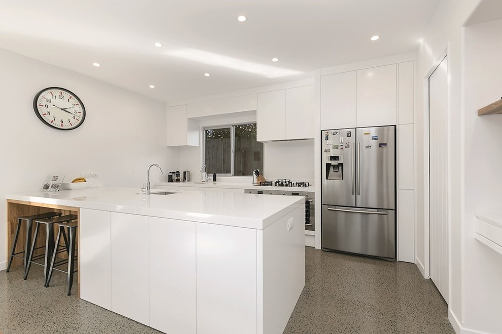 Medium sized contemporary u-shaped kitchen/diner in Wellington with a built-in sink, recessed-panel cabinets, white cabinets, white splashback, stainless steel appliances, concrete flooring, an island, multi-coloured floors and white worktops.