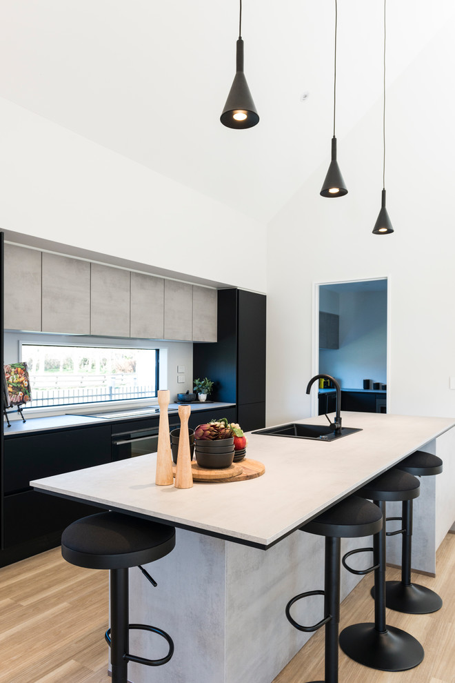 Mid-sized minimalist galley laminate floor and brown floor kitchen pantry photo in Christchurch with a drop-in sink, flat-panel cabinets, black cabinets, laminate countertops, white backsplash, window backsplash, stainless steel appliances and an island
