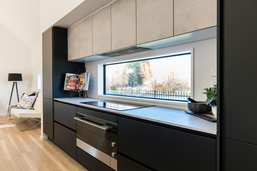Foto di una cucina moderna di medie dimensioni con lavello da incasso, ante lisce, ante nere, top in laminato, paraspruzzi bianco, paraspruzzi a finestra, elettrodomestici in acciaio inossidabile, pavimento in laminato e pavimento marrone