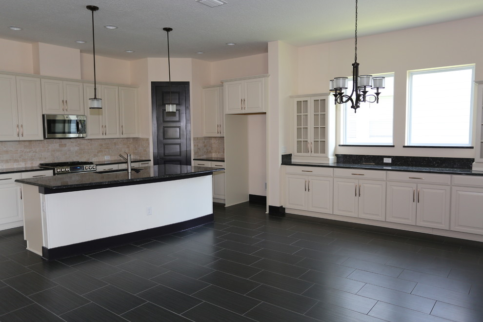 Klassisk inredning av ett mellanstort kök, med en undermonterad diskho, luckor med upphöjd panel, vita skåp, granitbänkskiva, beige stänkskydd, stänkskydd i travertin, rostfria vitvaror, klinkergolv i porslin, en köksö och svart golv