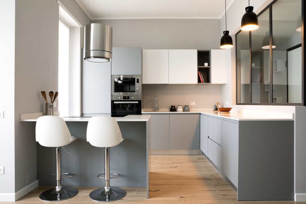 Moderne Küche in L-Form mit flächenbündigen Schrankfronten, grauen Schränken, Küchengeräten aus Edelstahl, hellem Holzboden, Halbinsel, beigem Boden und weißer Arbeitsplatte in Sonstige