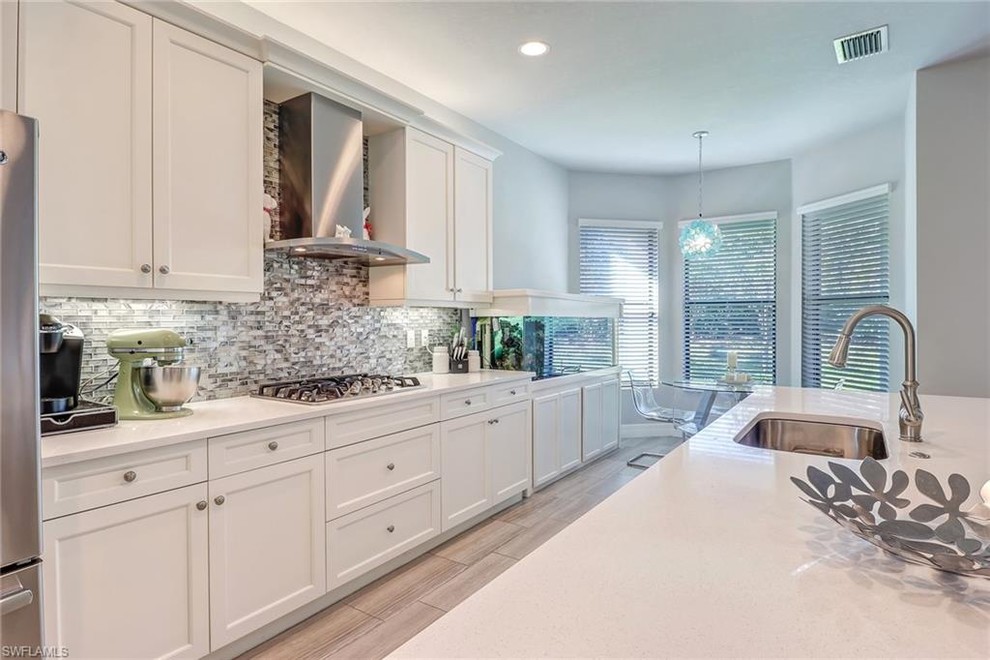 Example of a large trendy l-shaped light wood floor and beige floor open concept kitchen design in Miami with an undermount sink, recessed-panel cabinets, white cabinets, quartz countertops, multicolored backsplash, matchstick tile backsplash, stainless steel appliances, an island and white countertops