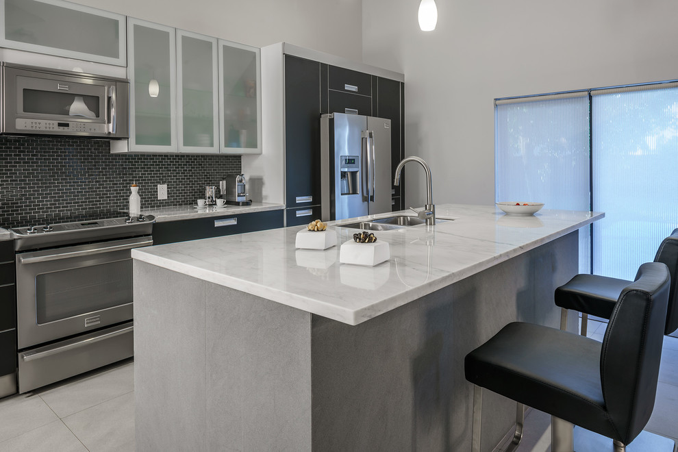 Example of a mid-sized minimalist single-wall porcelain tile kitchen pantry design in Miami with an undermount sink, flat-panel cabinets, black cabinets, marble countertops, gray backsplash, glass tile backsplash, stainless steel appliances and an island
