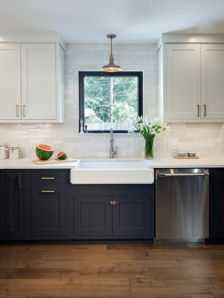 Bild på ett lantligt vit vitt kök, med en rustik diskho, skåp i shakerstil, blå skåp, bänkskiva i kvarts, vitt stänkskydd, stänkskydd i keramik, rostfria vitvaror, mellanmörkt trägolv och en halv köksö