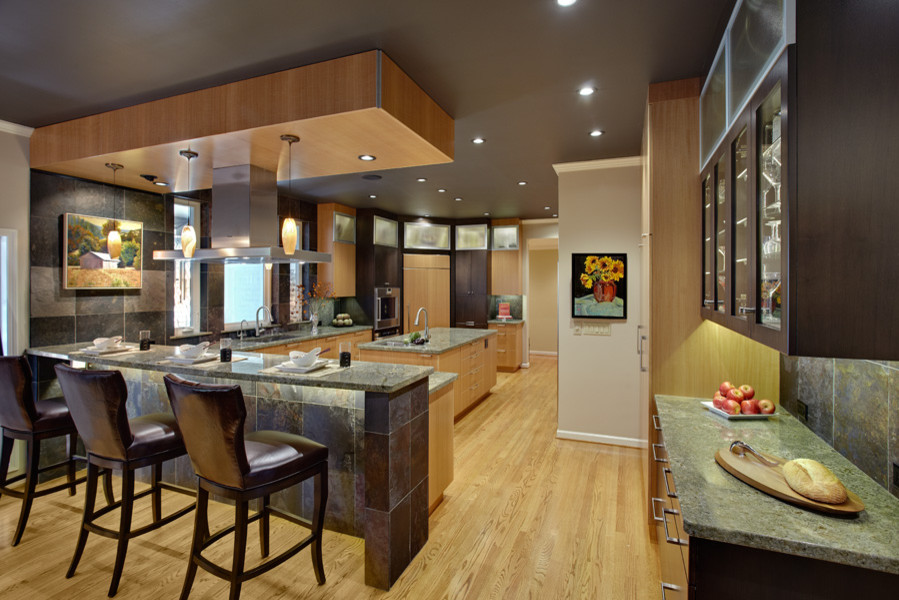 Mid-sized trendy l-shaped light wood floor enclosed kitchen photo in Sacramento with an undermount sink, flat-panel cabinets, light wood cabinets, granite countertops, gray backsplash, stone tile backsplash, stainless steel appliances and a peninsula