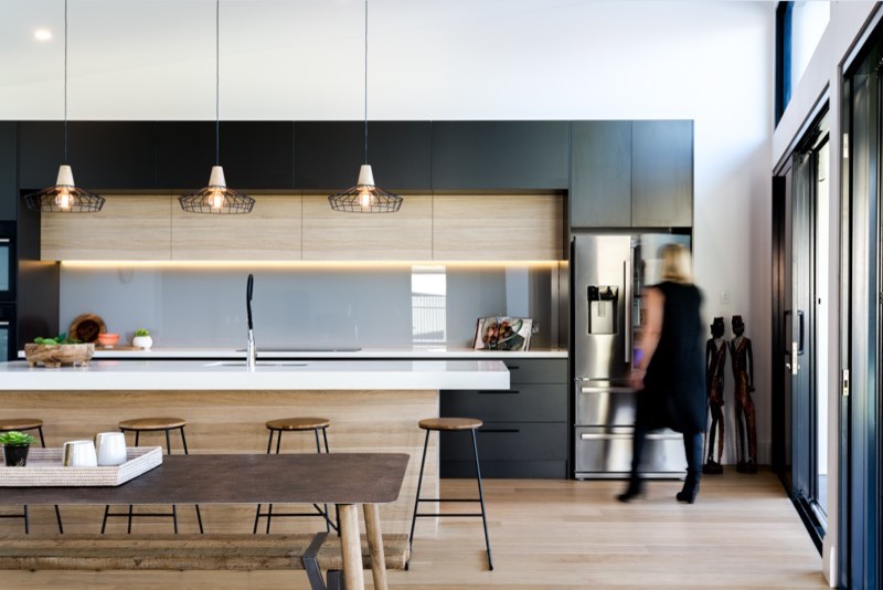 Foto på ett minimalistiskt kök, med släta luckor, grå skåp, marmorbänkskiva, grått stänkskydd, glaspanel som stänkskydd, svarta vitvaror, ljust trägolv och en köksö