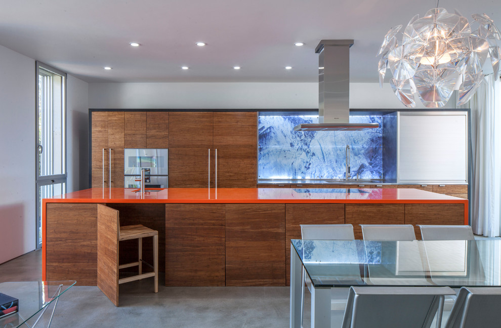 Modern inredning av ett orange oranget kök, med en undermonterad diskho, släta luckor, skåp i mellenmörkt trä, integrerade vitvaror, betonggolv, en köksö, grått golv och blått stänkskydd
