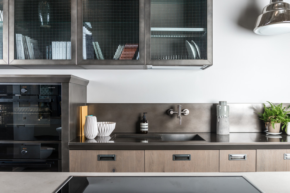 Large scandi kitchen/diner in London with an integrated sink, medium wood cabinets, composite countertops, grey splashback, stainless steel appliances and a breakfast bar.