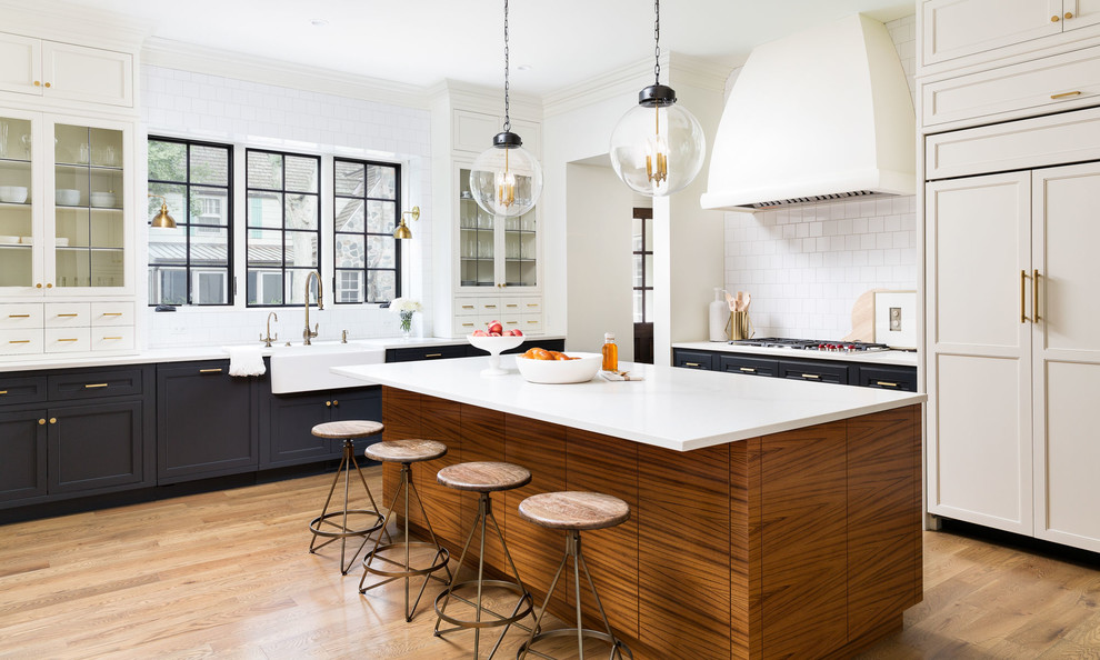 Inspiration for a mid-sized transitional light wood floor kitchen remodel in Detroit with white cabinets, marble countertops, white backsplash, ceramic backsplash, an island, a farmhouse sink, paneled appliances and glass-front cabinets