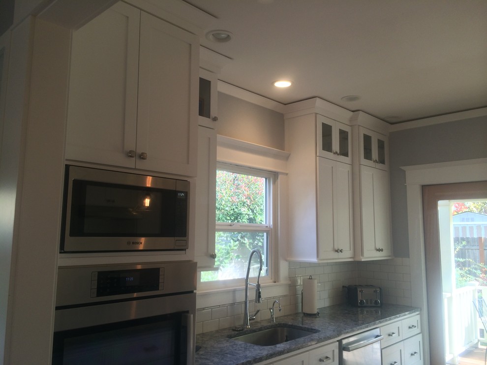 Exempel på ett stort klassiskt kök, med en undermonterad diskho, luckor med infälld panel, vita skåp, granitbänkskiva, vitt stänkskydd, stänkskydd i tunnelbanekakel, rostfria vitvaror, mellanmörkt trägolv och en köksö
