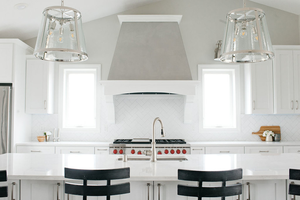 Bild på ett stort vintage vit vitt kök, med en undermonterad diskho, skåp i shakerstil, vita skåp, vitt stänkskydd, rostfria vitvaror, en köksö, bänkskiva i kvartsit, stänkskydd i tunnelbanekakel, mellanmörkt trägolv och brunt golv