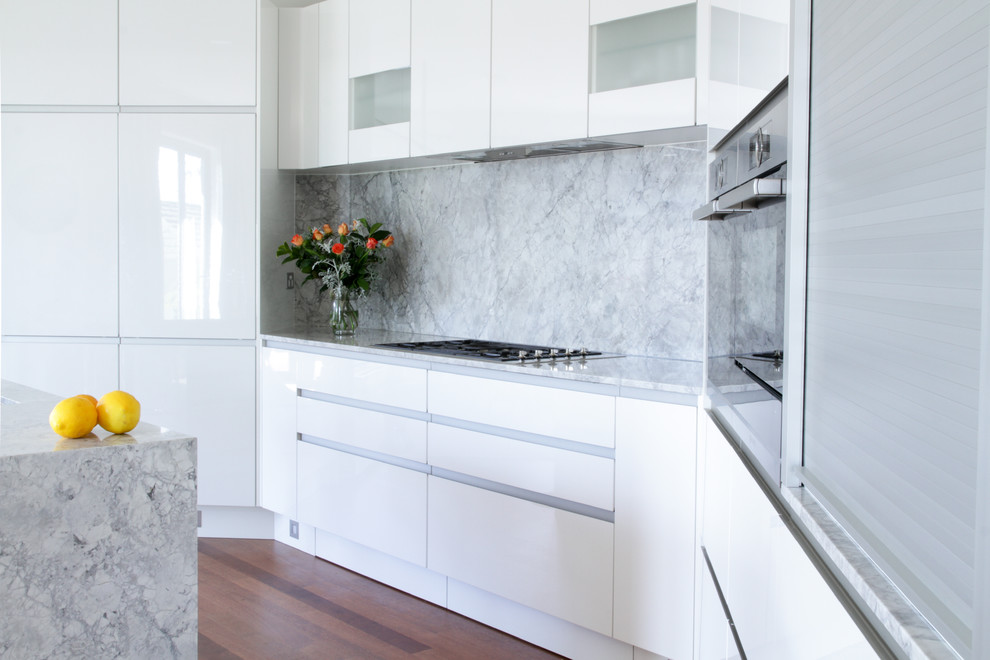 Foto på ett stort funkis kök, med en undermonterad diskho, släta luckor, vita skåp, marmorbänkskiva, grått stänkskydd, stänkskydd i marmor, rostfria vitvaror, laminatgolv, en köksö och brunt golv