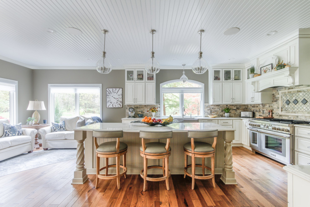 Inspiration for a large transitional l-shaped medium tone wood floor and brown floor eat-in kitchen remodel in Detroit with a farmhouse sink, raised-panel cabinets, white cabinets, quartz countertops, beige backsplash, travertine backsplash, stainless steel appliances, an island and white countertops
