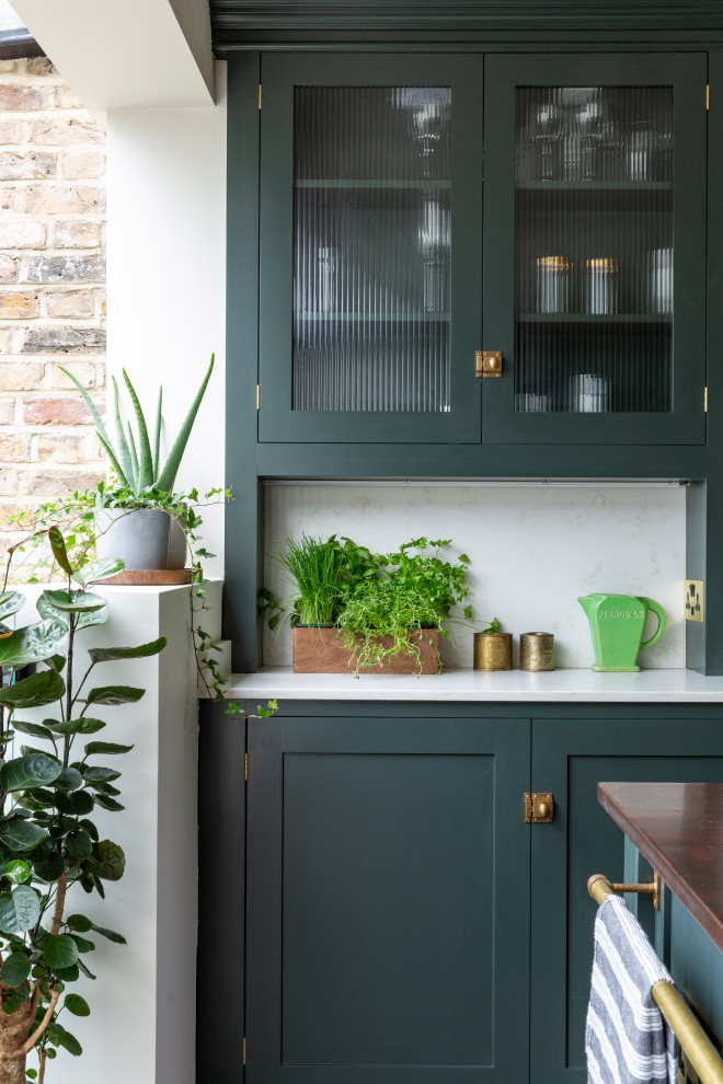ロンドンにある高級な中くらいなエクレクティックスタイルのおしゃれなキッチン (エプロンフロントシンク、シェーカースタイル扉のキャビネット、緑のキャビネット、珪岩カウンター、メタリックのキッチンパネル、大理石のキッチンパネル、黒い調理設備、無垢フローリング、茶色い床、白いキッチンカウンター) の写真