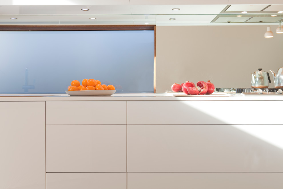 Moderne Küche mit flächenbündigen Schrankfronten, weißen Schränken, Mineralwerkstoff-Arbeitsplatte, Küchenrückwand in Metallic und Rückwand aus Spiegelfliesen in Sydney