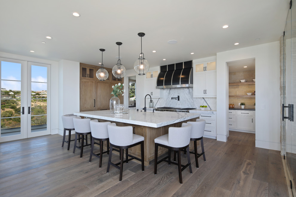 Transitional medium tone wood floor and brown floor open concept kitchen photo in Los Angeles with a farmhouse sink, shaker cabinets, light wood cabinets, white backsplash, stainless steel appliances and an island