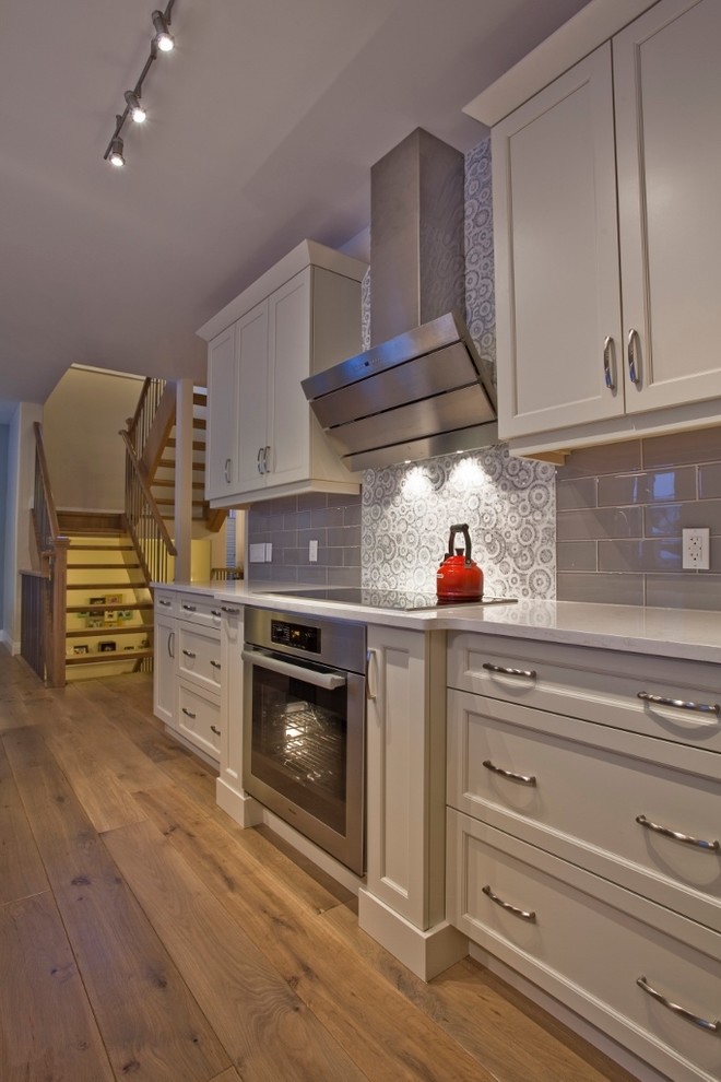 Large trendy l-shaped light wood floor eat-in kitchen photo in Edmonton with an undermount sink, shaker cabinets, white cabinets, quartz countertops, gray backsplash, subway tile backsplash, stainless steel appliances and an island