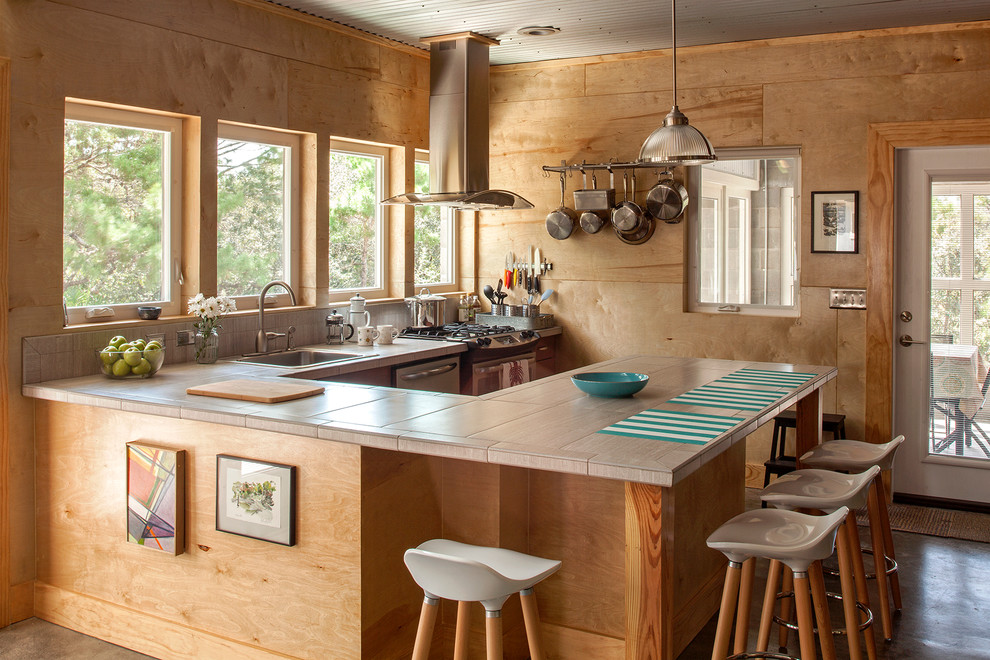 Inspiration for a mid-sized industrial u-shaped concrete floor open concept kitchen remodel in Miami with light wood cabinets, tile countertops, stainless steel appliances, a peninsula, a drop-in sink, beige backsplash and porcelain backsplash