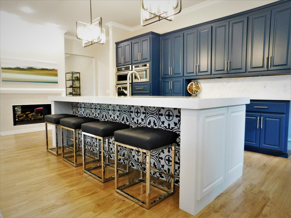 Bild på ett stort vintage vit vitt kök, med en undermonterad diskho, luckor med upphöjd panel, blå skåp, bänkskiva i kvarts, vitt stänkskydd, stänkskydd i marmor, rostfria vitvaror, mellanmörkt trägolv, en köksö och brunt golv