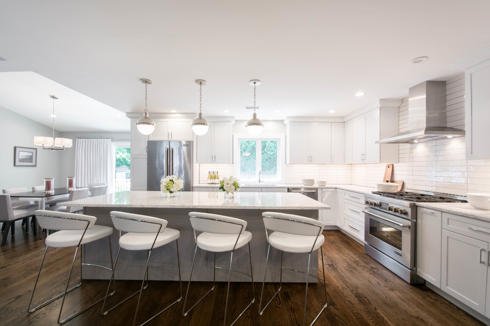 Design ideas for a large modern l-shaped open plan kitchen in Providence with a submerged sink, shaker cabinets, white cabinets, white splashback, stainless steel appliances, dark hardwood flooring, an island, white worktops, ceramic splashback, brown floors and engineered stone countertops.